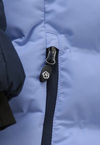 Lys blå pufferjakke-sektion med en lynlås med en sort trækkrog, omkranset af en mørk marineblå panel, der viser en glat, mat struktur.