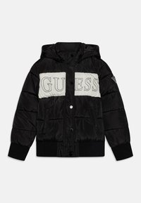 Czarna kurtka puchowa z kapturem, białym panelem na piersi z napisem „GUESS”, zatrzaskami, ściągaczami przy mankietach oraz naszywką z logo na rękawie.