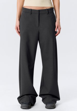 Pantalon gris foncé à rayures fines, taille basse et jambes larges, porté avec des baskets noires et un haut court beige.