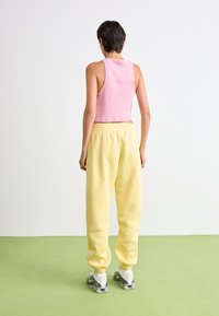 Lyserød ribbet tanktop og løse gule sweatpants med elastisk talje, parret med grå og hvide sneakers, set fra bagtil.
