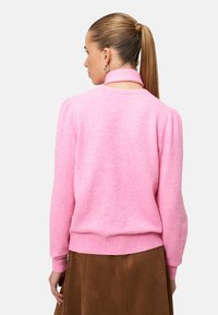 Pink knitted sweater with a ribbed collar, puffed sleeves, and fitted waistband, paired with a brown suede skirt. Textured fabric.