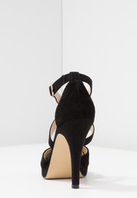 Sandales à talons hauts en daim noir avec une lanière à la cheville, dos ouvert et un design à bout pointu. Le talon surélevé rehausse l'élégance.