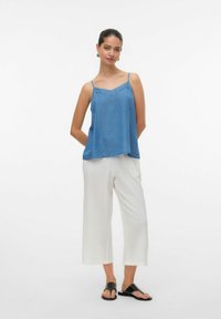 Top blu senza maniche con spalline sottili, scollatura dritta e orlo. Abbinato a pantaloni bianchi a gamba larga e sandali neri.