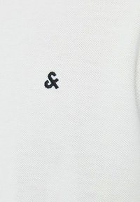 Witte polo shirt van een gestructureerde stof met een klein zwart geborduurd logo aan de linkerkant. Eenvoudig ontwerp zonder extra patronen.
