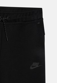 Pantalons de survêtement noirs Nike avec taille élastique, fermeture à cordon, et un logo subtil imprimé en gris foncé sur la jambe gauche.