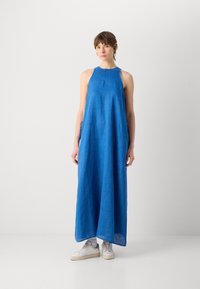Blå linne ärmlös maxiklänning med en avslappnad passform. Har en hög halsringning och sidospaltnar, kombinerat med vita låga sneakers.