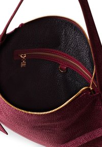 Red textured handbag with a zippered opening, featuring a black inner lining and a gold zipper detail, offering an inner pocket for storage.
