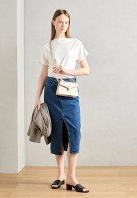 White short-sleeve top, blue denim skirt with front slit, black block-heeled sandals, holding a plaid jacket and beige handbag.