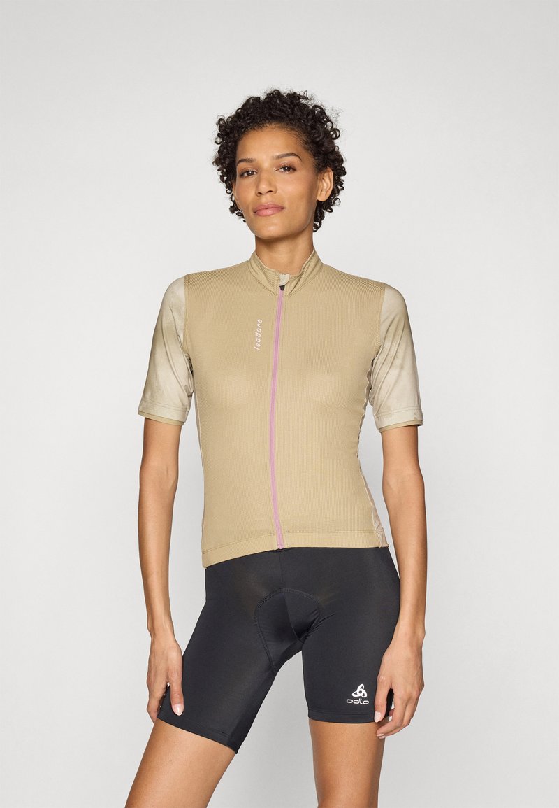 Maglia da ciclismo a maniche corte di colore sabbia con cerniera rosa, tessuto testurizzato; abbinata a pantaloni corti da ciclismo neri, con logo sulla gamba sinistra.