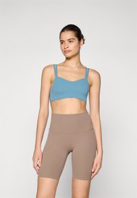Sport BH i blått med tynne stropper, kombinert med høytalede brune sykkelshorts. Glatt tekstur og tettsittende design for komfort under aktiviteter.