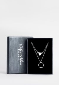 Sølvbelagt halskæde med en trekantet vedhæng og en cirkulær charm, præsenteret i en sort fløjlbeklædt æske med en struktureret sølvoverflade.