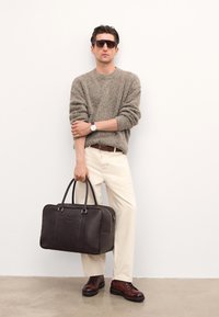 Braunā ādas soma ar divām rokturiem, apvienota ar teksturētu bēšu džemperi, krēmkrāsas biksēm un brūnām šņorējamām zālēm. Gaismas fons.