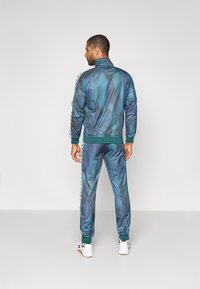 Chándal en gradiente azul-verde con puños y dobladillo acanalados. Presenta franjas laterales llamativas y un cuello alto. El material parece suave y elegante.