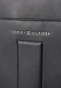 Black leather product with a textured finish, featuring the "TOMMY HILFIGER" logo in silver. Includes a stitched accent detail.