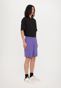 Camiseta negra de manga corta combinada con pantalones cortos de algodón morados, con una cinturilla elástica. Zapatillas blancas con detalles en negro completan el look.
