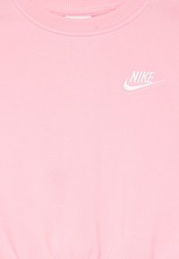 Rožinė medvilninė džemperis su apvalia iškirpte, kuriame viršutiniame kairiajame kampe yra baltas išsiuvinėtų Nike logotipas. Lygus paviršius.