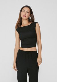 Top crop nero aderente a spalla unica realizzato in tessuto liscio; abbinato a pantaloni neri larghi con coulisse regolabile.