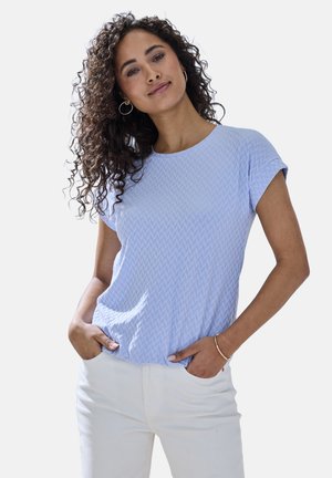 Hellblaues Kurzarmoberteil mit strukturiertem Zickzackmuster, rundem Ausschnitt und lockerer Passform, kombiniert mit weißen Hosen.