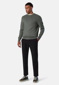 Felpa verde oliva con logo in rilievo, collezione girocollo, polsini a costine, abbinata a pantaloni neri slim-fit e sneakers verde/nera.