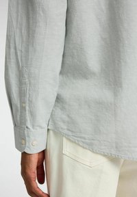 Lichtgrijs overhemd met lange mouwen en een relaxte pasvorm, voorzien van knopen op de mouwen en een licht gebogen zoom, gecombineerd met off-white broek.