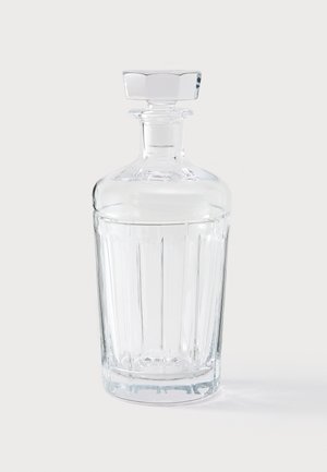 Decantador de vidrio transparente con diseño de costillas verticales, tapón hexagonal y cuello cilíndrico liso. Refleja la luz, mostrando claridad.