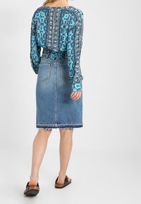 Top lungo a maniche lunghe blu con motivo e vestibilità comoda, abbinato a una gonna a matita in denim con orlo grezzo e tasche posteriori. Calzature marroni slip-on.