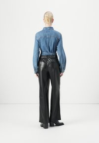 Denim overhemd met lange mouwen en een aansluitende taille, gecombineerd met zwarte leren wijde broek en leren laarzen met hak. Glad textuur en contrasterende kleuren.