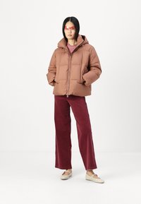 Brun puffjakke med glidelås foran, hette og quiltet design, sammen med burgunder vide cordbukser og beige sko.