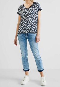 Top à manches courtes en zigzag bleu marine et crème avec un col en V, assorti à un jeans cropped en denim clair et des baskets blanches.