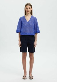 Blå, luftig v-ringad topp med korta ärmar, kombinerad med mörkblå shorts och svarta flip-flops. Texturerad tyg med lös passform.