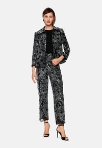 Sequined black blazer and pants set with floral patterns, featuring a ribbed black top and strappy high heels. Textured fabric and lace accents.