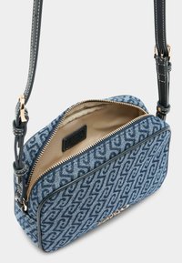 Niebieska torba na ramię z denimu z pikowanym wzorem, złotym zamkiem błyskawicznym i czarnymi skórzanymi akcentami. Wnętrze wykonane z beżowej tkaniny z metką logo.