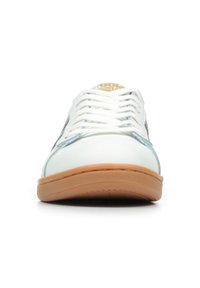 Sneaker bianca con suola in gomma beige, con accenti in suede grigio, lacci bianchi e un logo circolare sulla linguetta. Design corto e a taglio basso.