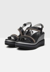 Black platform sandals with metallic accents, featuring crisscross straps and an adjustable ankle buckle. Textured detailing on straps.
