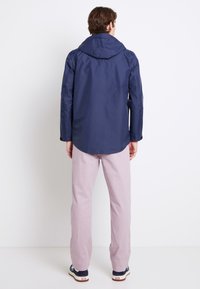 Navy waterproof jacket with a hood, featuring long sleeves and a buttoned cuff. Light pink lightweight pants, paired with blue sneakers.