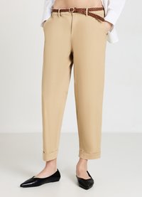 Pantaloni beige con una vestibilità dritta e orli arrotolati, dotati di tasche laterali e una cintura intrecciata marrone. Indossati con delle ballerine nere a punta.