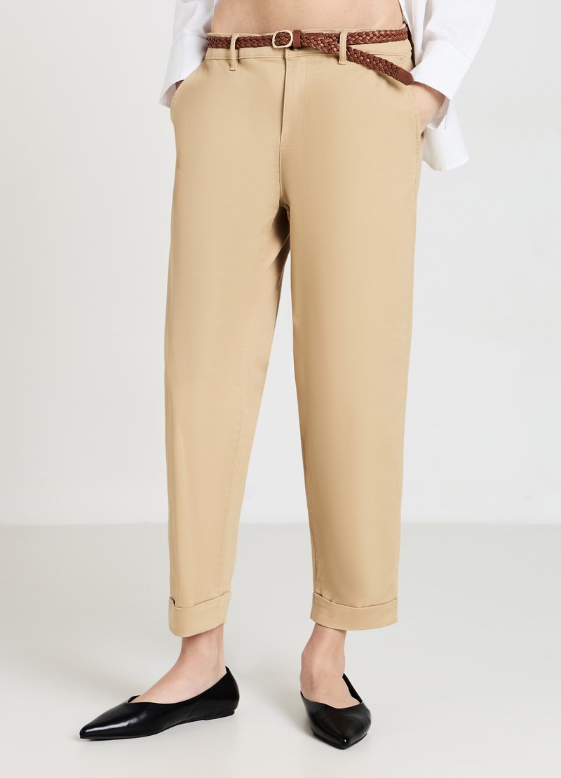 Pantaloni beige con una vestibilità dritta e orli arrotolati, dotati di tasche laterali e una cintura intrecciata marrone. Indossati con delle ballerine nere a punta.