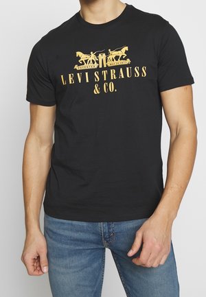 T-shirt en coton noir avec un col rond, présentant un design graphique doré de chevaux et le texte "LEVI STRAUSS & CO." en lettres grasses.