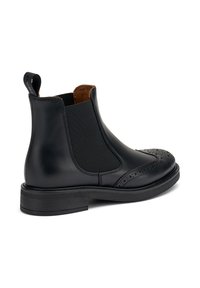 Bota Chelsea de cuero negro con paneles laterales elásticos, detalles de brogue en la puntera y una suela plana de goma. Textura suave y diseño elegante.