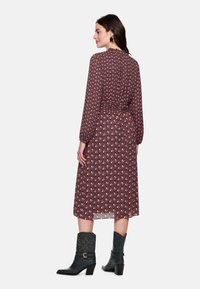 Dunkelrotes Kleid mit Rautenmuster, langen Ärmeln und geraffter Taille. Kombiniert mit schwarzen Stiefeletten mit einer Schnallenriemen.