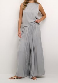 Ljust grå tvådelad outfit bestående av en ärmlös topp och vida byxor med mjukt, flödande tyg, slät textur och avslappnad passform.