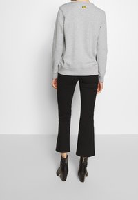 Gray sweatshirt with crew neck, ribbed cuffs, and hem. Paired with black flared pants and ankle boots featuring a chunky heel and zipper detail.
