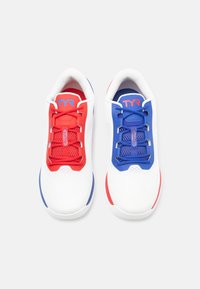 Witte sneakers met rode en blauwe accenten, voorzien van meshpanelen, contrasterende veters en een gevoerde kraag. Logo zichtbaar op de tong.
