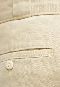 Beżowa bawełniana tkanina o fakturowanym splocie, z małą kieszonką naszytą i pojedynczym, jasnym guzikiem.