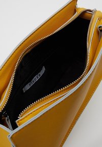 Borsa a mano in pelle gialla con superficie testurizzata, cerniera argentata e fodera nera. Etichetta interna visibile con il nome del marchio "PIECES".