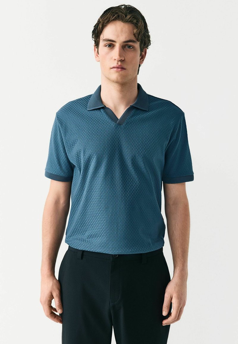 Polo de color azul oscuro, tejido texturizado, con cuello en V y collar en contraste. Combinado con pantalones negros, de manga corta y corte regular.