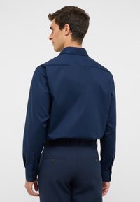Camicia a maniche lunghe blu navy in tessuto morbido, con colletto standard e polsini abbottonati, abbinata a pantaloni blu scuro su misura.