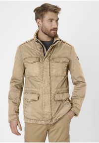 Beige utility jacket made of lightweight fabric, featuring two chest pockets, an adjustable collar, and a cinched waist for a fitted look.