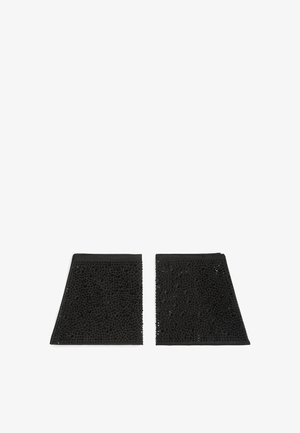 Protezioni per caviglia in tessuto nero con superficie texturizzata e piccole perle, caratterizzate da un design angolare e un bordo esterno liscio.