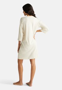 Světle béžová noční košile po kolena s volným střihem, tříčtvrtečními rukávy a měkkou strukturou. Jednoduchý design bez výrazných vzorů či akcentů.